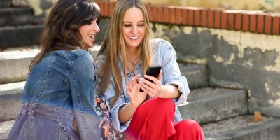 Two women sharing social media with smart phone outdoors