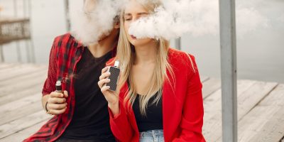Stylish young couple with vape in a city