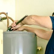 Adult male using a wrench to make adjustments on top of a hot water heater