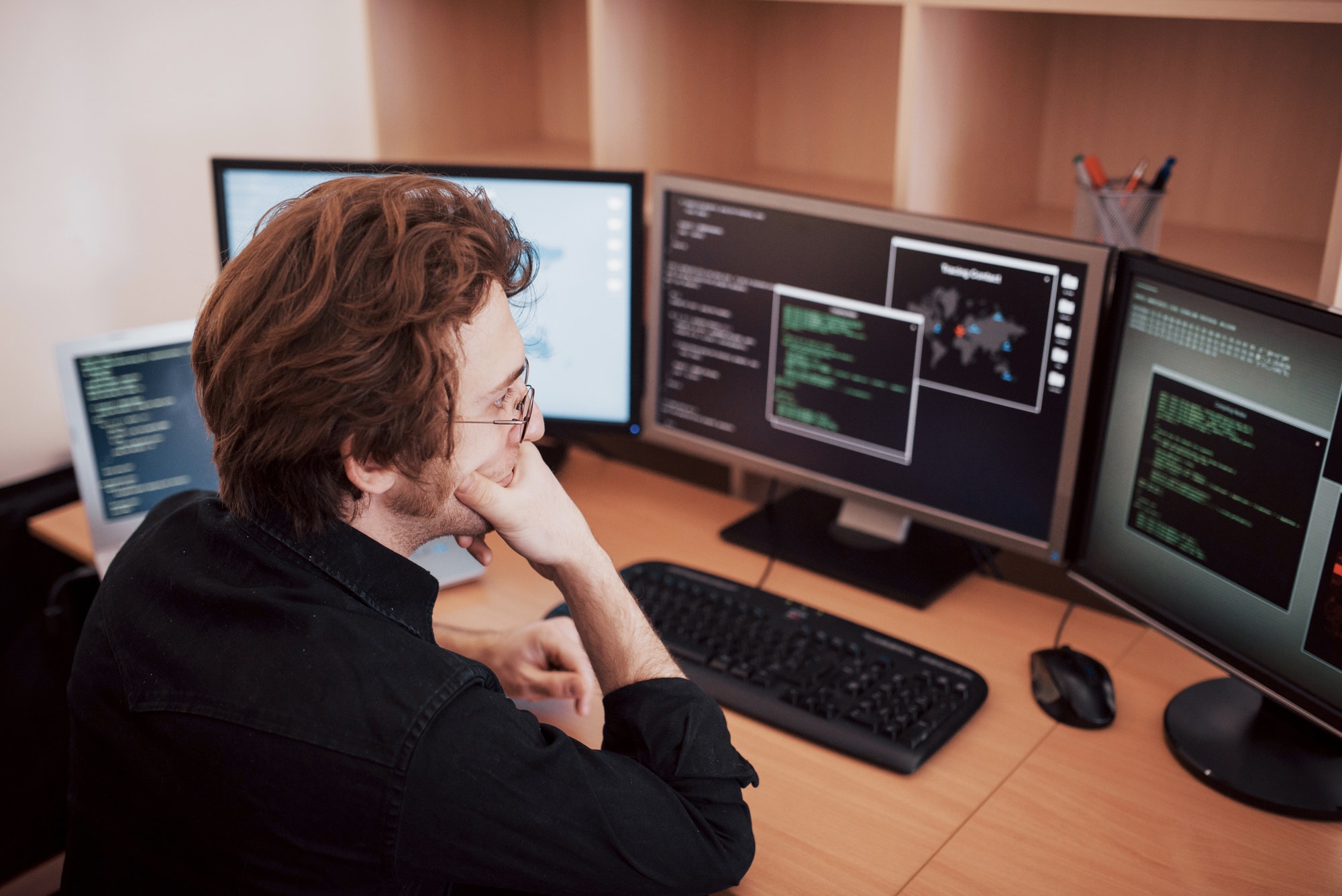 Male programmer working on desktop computer with many monitors at office in software develop company
