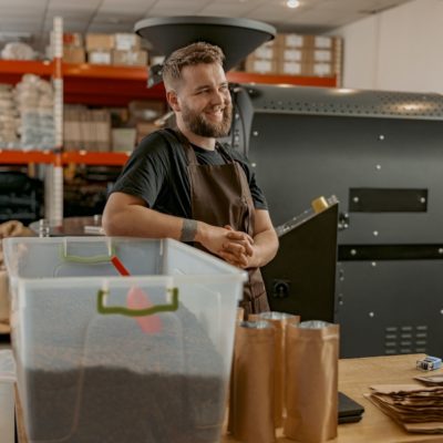 Portrait of smiling business owner on background of own small coffee factory looking away