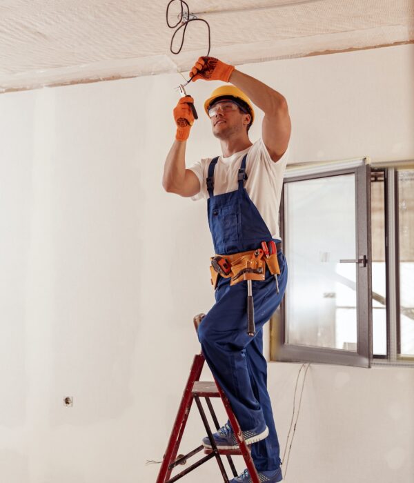 Smiling electrician fixing electric cable on ceiling